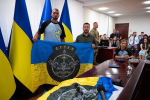Президент України Володимир Зеленський зустрівся з переможцями ІІІ Європейських ігор, на яких збірна України виборола третє загальнокомандне місце. Чемпіон із таїландського боксу Муей Тай Олег Приймачов передав Володимиру Зеленському український прапор із підписами бійців одного зі спецпідрозділів, 8 вересня 2023 року.